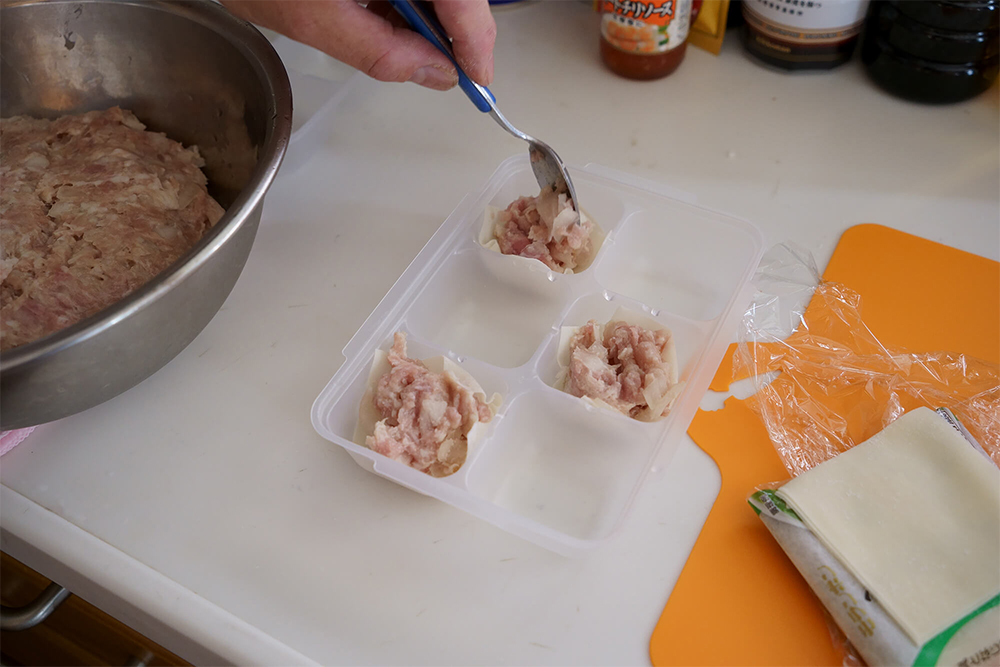 (E)皮は窪みに1つおきに敷き、肉種をスプーンで詰めていく。皮をすべて敷くと、皮が手にくっつくなどして詰めにくい。