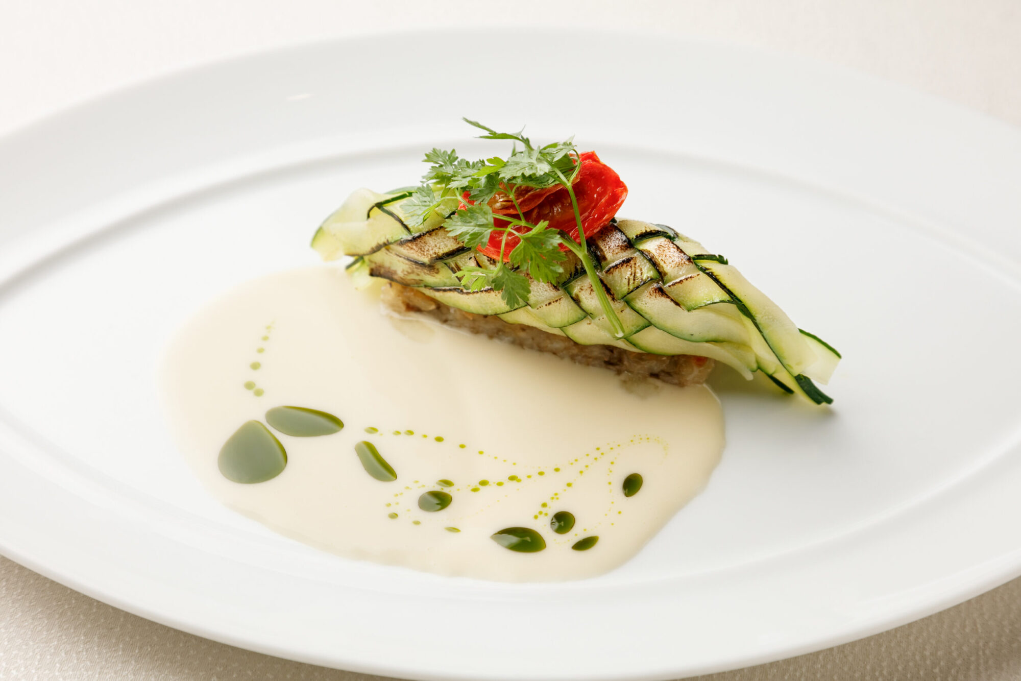 「ラングスティーヌのクルージェット包み」。マリネしたラングスティーヌ（手長エビ）をリボン状にスライスして編み上げたクルージェット（ズッキーニ）で包み、蒸した後、あさりだしのソースで仕上げた一皿。エビの甘味とアサリの磯の香りが重なり、穏やかで優しい味わい。